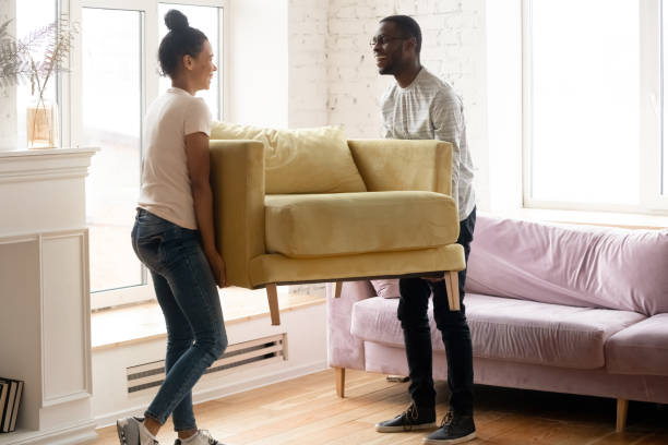 Young happy african american couple moving and carry table. Attractive family of diverse woman and man relocation furniture in new home. Husband and wife perform permutation.